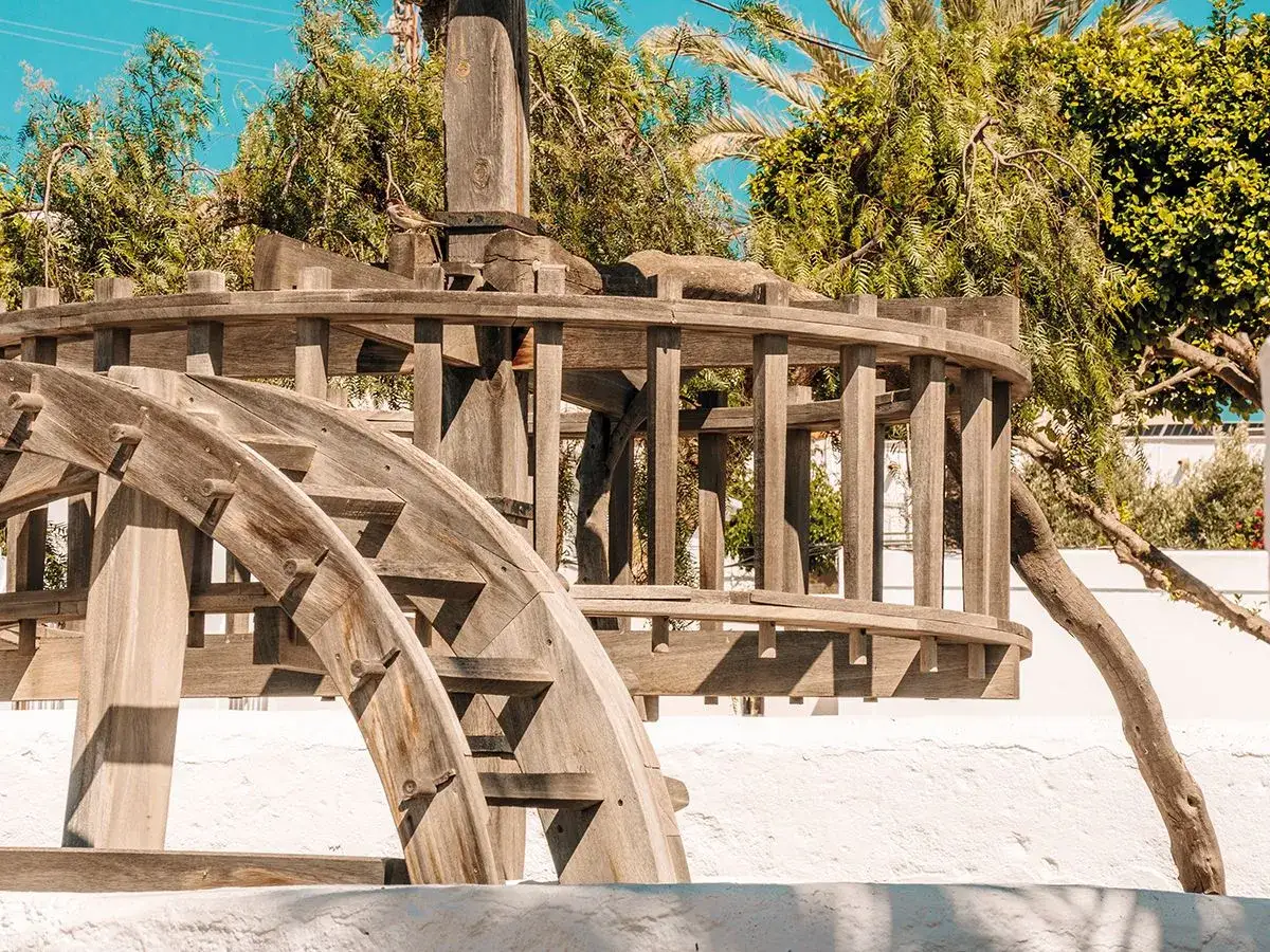 Antigua noria de madera, parte de lo que ver en el pozo de los frailes. Rodeada de vegetación y cielo azul.