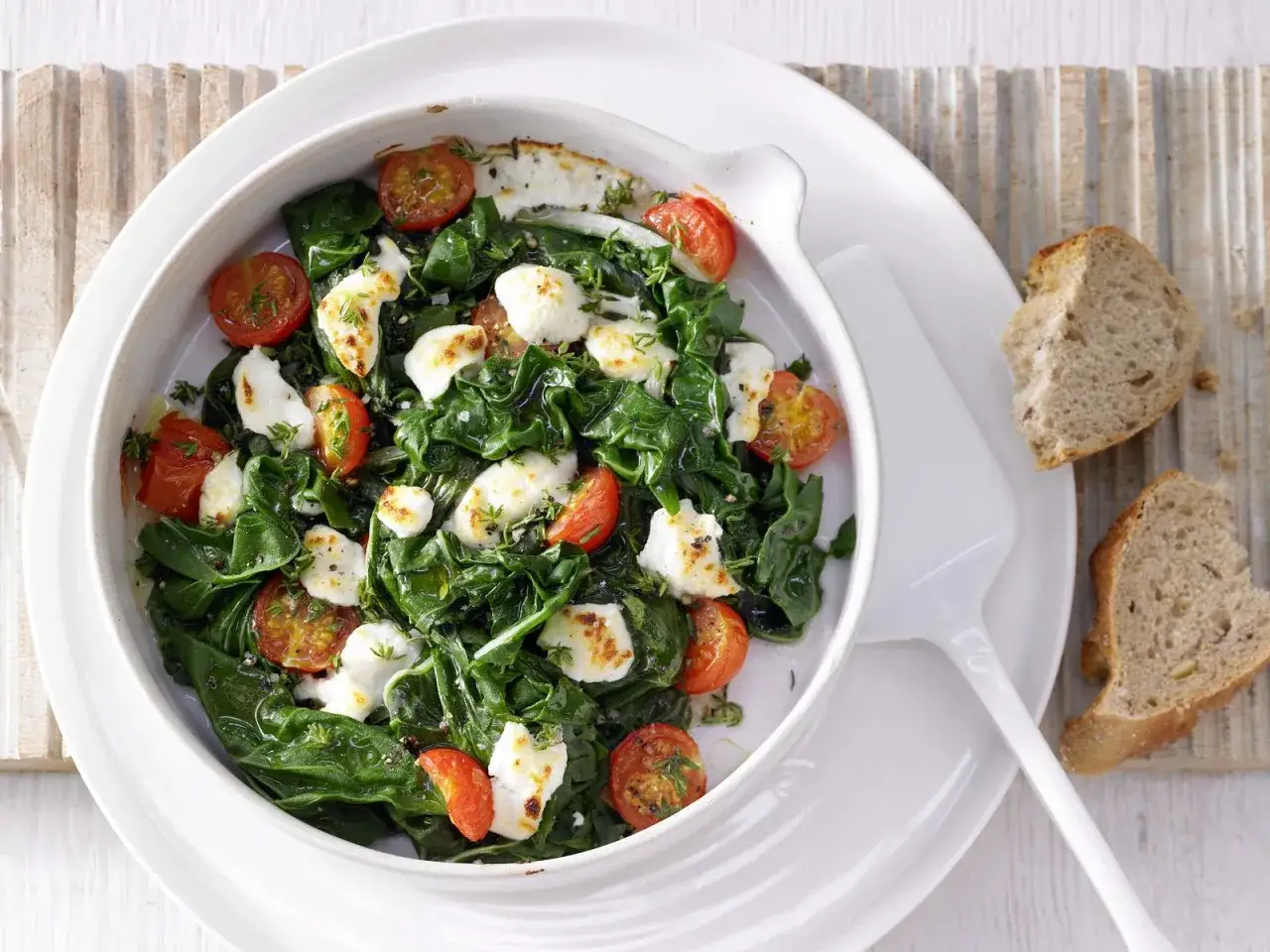 Ein k&ouml;stliches Mangold-Rezept mit Kirschtomaten und Mozzarella, serviert in einer Auflaufform. Dazu gibt es knuspriges Brot.