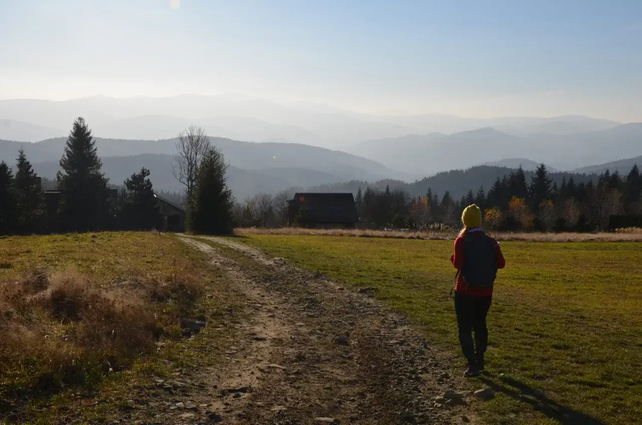 Widok na pasmo górskie Koskowa Góra. Turystka w żółtej czapce i czerwonej kurtce z plecakiem podziwia krajobraz.
