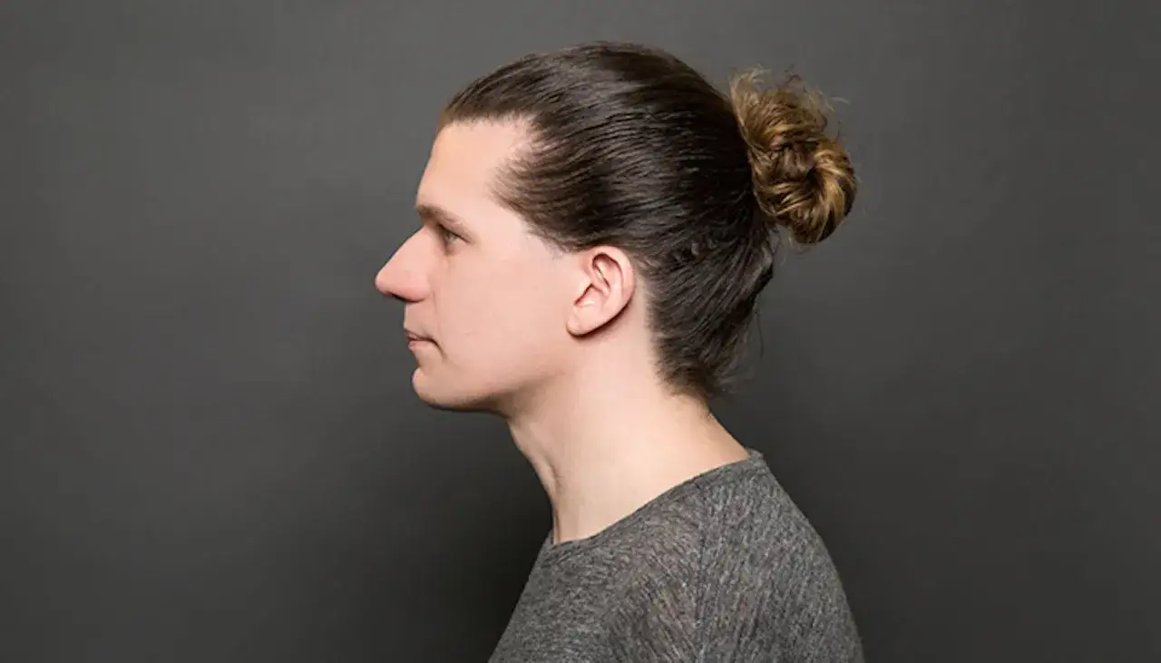 Profil d'un homme avec un man bun, cheveux bruns attachés en chignon.