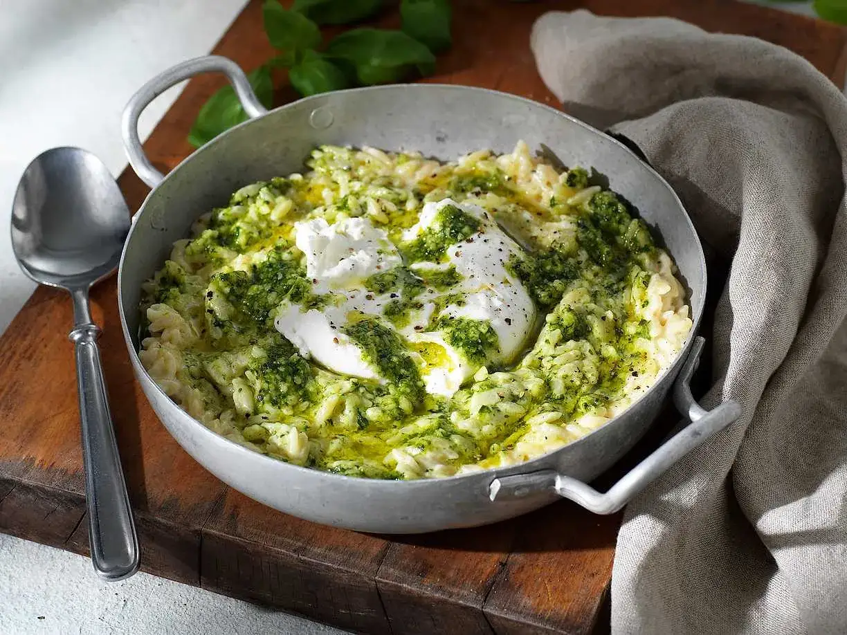 En skål med pasta som ser ut som ris, toppad med krämig burrata och grön pesto. En utsökt rätt som ser ut att vara gjord med kärlek.