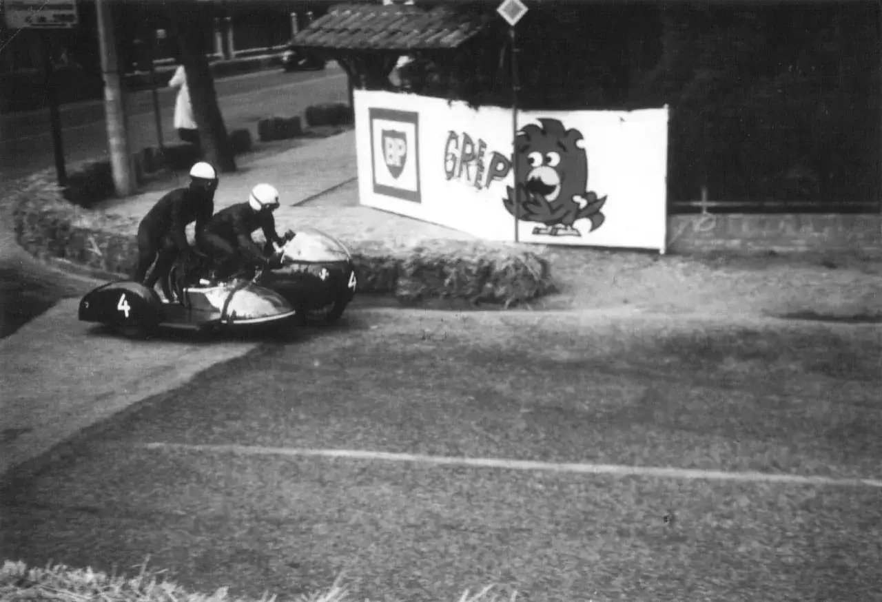 Equipaggio in gara con sidecar, numero 4, durante le corse di motociclistiche. Sullo sfondo, un cartellone pubblicitario con un personaggio dei cartoni animati.