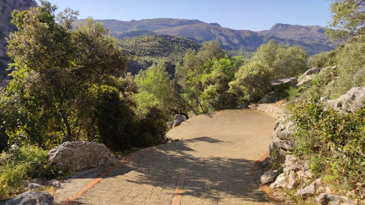 Ein gepflasterter Weg f&uuml;hrt zu einem Aussichtspunkt mit Blick auf die Berge. Die **Cueva del Gato** ist vielleicht in der N&auml;he, versteckt im &uuml;ppigen Gr&uuml;n.