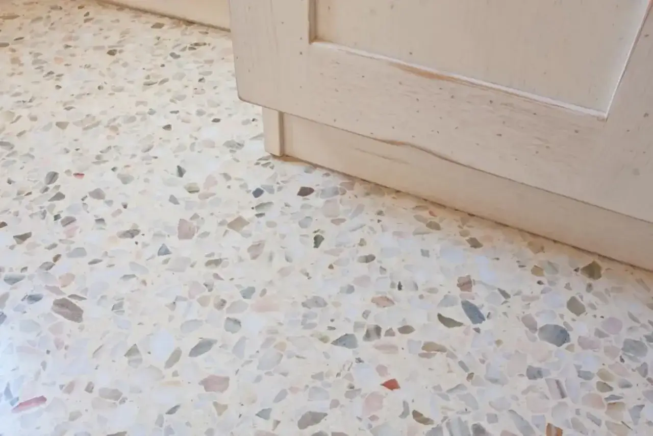 Un elegante **pavimento veneziana** con schegge di marmo colorate, accanto a un mobile in legno chiaro.