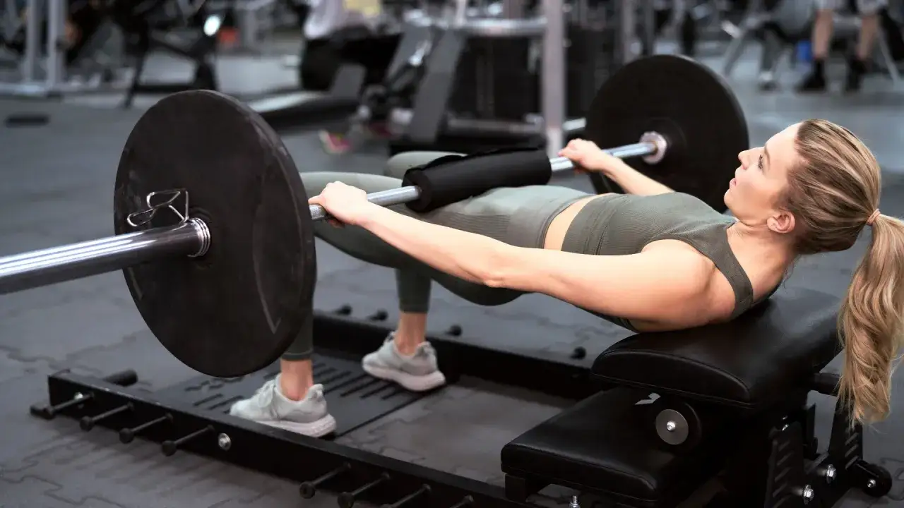 Donna in palestra esegue hip thrust con bilanciere, allenamento mirato per glutei perfetti.