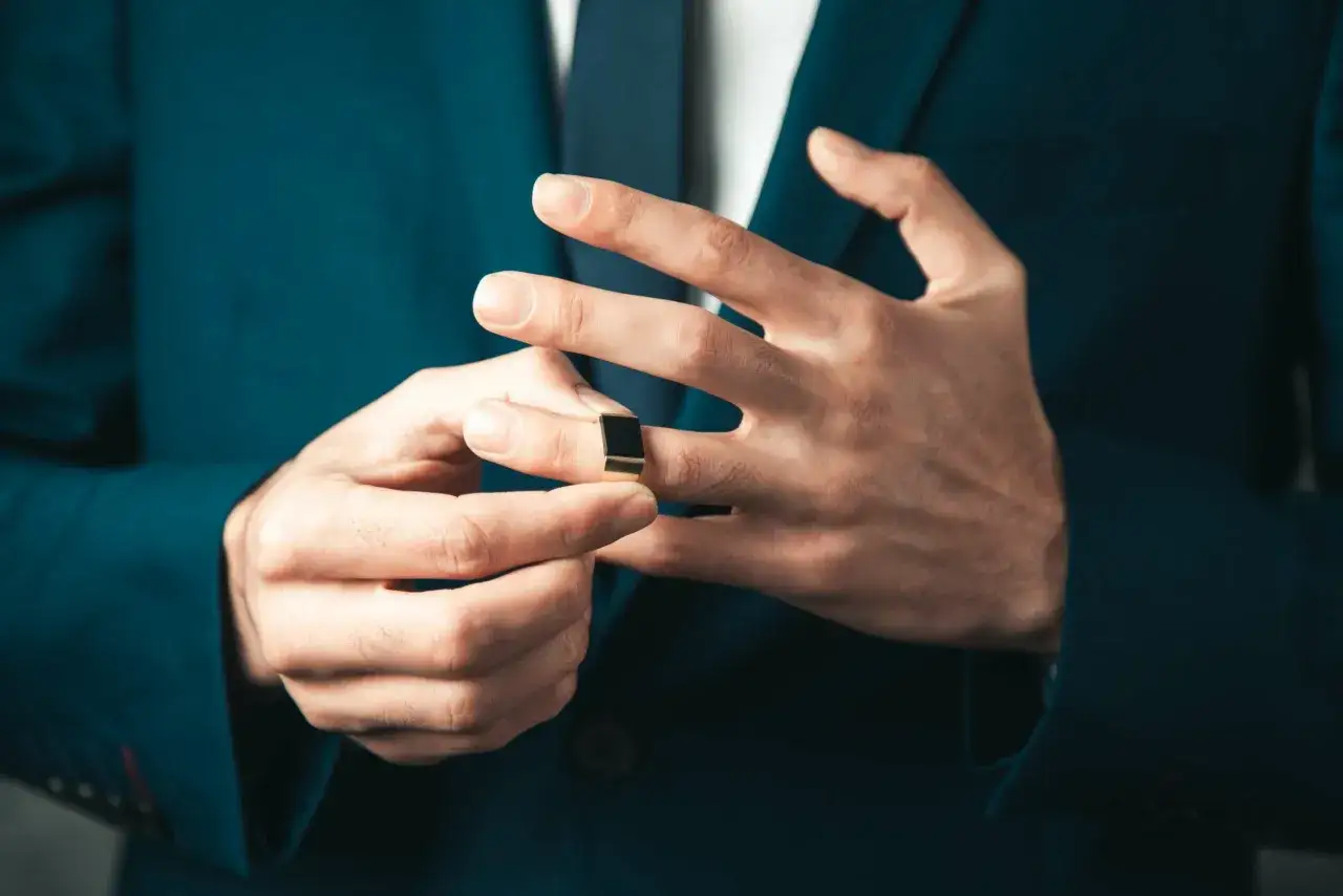 Mężczyzna w granatowej marynarce poprawia złoty sygnet z czarnym kamieniem. Dbałość o detale, jak zadbane paznokcie, to element męskiego manicure.