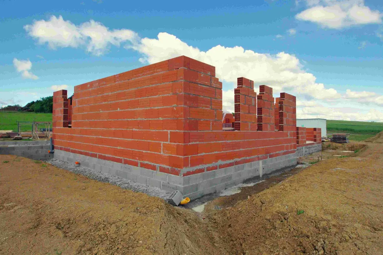 Budowa domu w toku: czerwone ściany z pustaków i betonowy fundament. Czas budowy domu zależy od wielu czynników.
