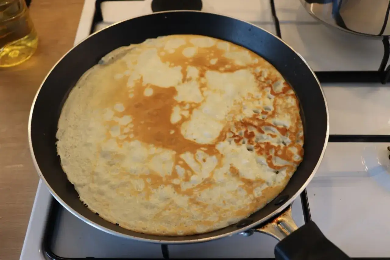 Smażony na patelni placek, idealny do domowego pan cake przepisu. Złocisty i rumiany, czeka na przewrócenie.