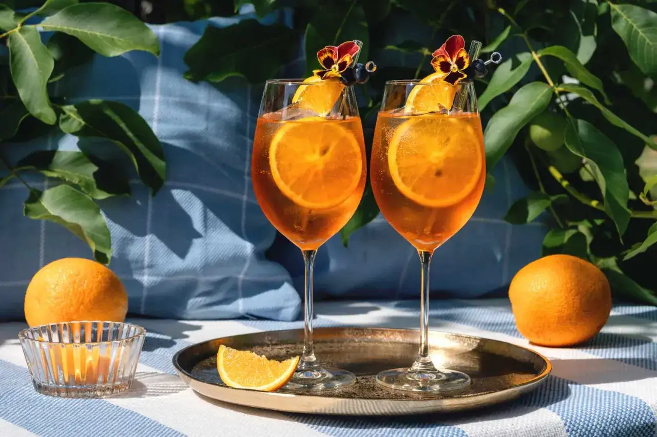 Dwa drinki z Aperolem, plastrem pomarańczy i kwiatkiem. Czy aperol można pić sam? Tak, ale z lodem i pomarańczą smakuje najlepiej.