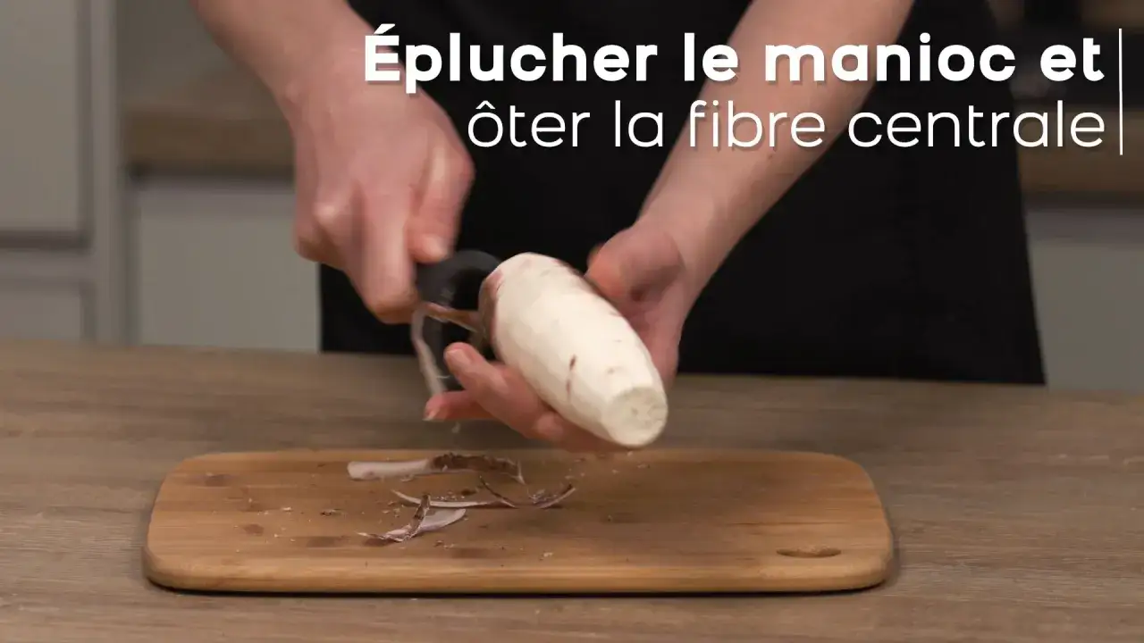 Préparation d'une recette de manioc : épluchage et retrait de la fibre centrale d'une racine de manioc sur une planche à découper.