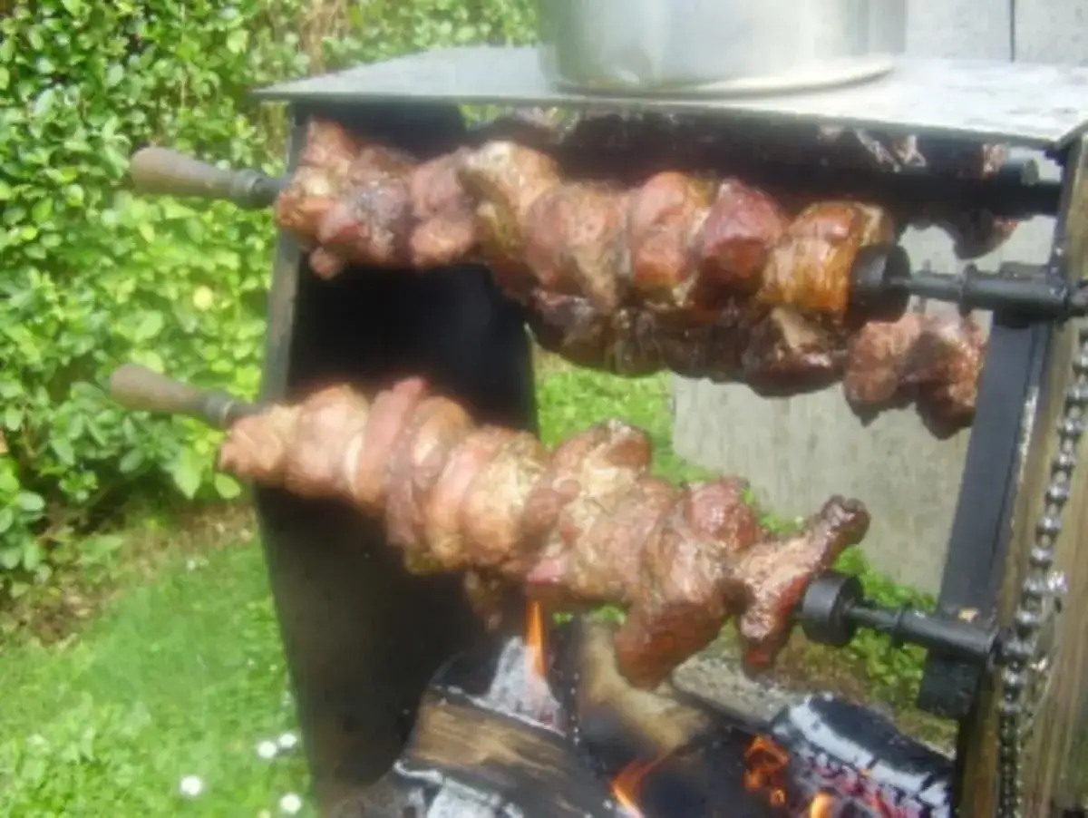 Zwei Spieße mit saftigem Mutzbraten drehen sich über offenem Feuer. Ein köstliches Rezept für den perfekten Grillgenuss.