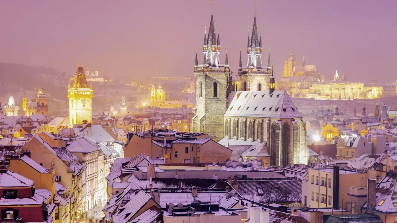 Prag im Winter: verschneite D&auml;cher und Kircht&uuml;rme im Abendlicht. Die Stadt erstrahlt in warmen T&ouml;nen, ein magischer Anblick.