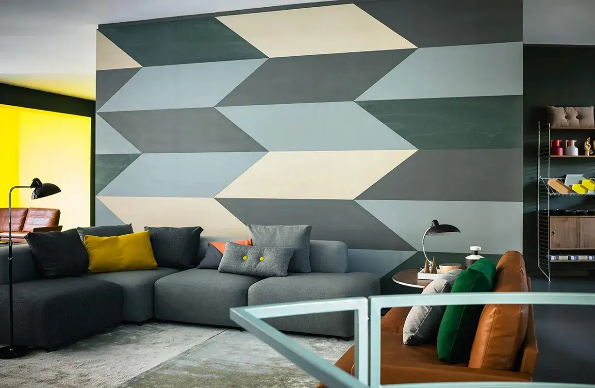 Un salon moderne avec un canapé gris, des coussins colorés et un mur orné d'un audacieux **modèle de peinture** géométrique en dégradé de bleus et gris.