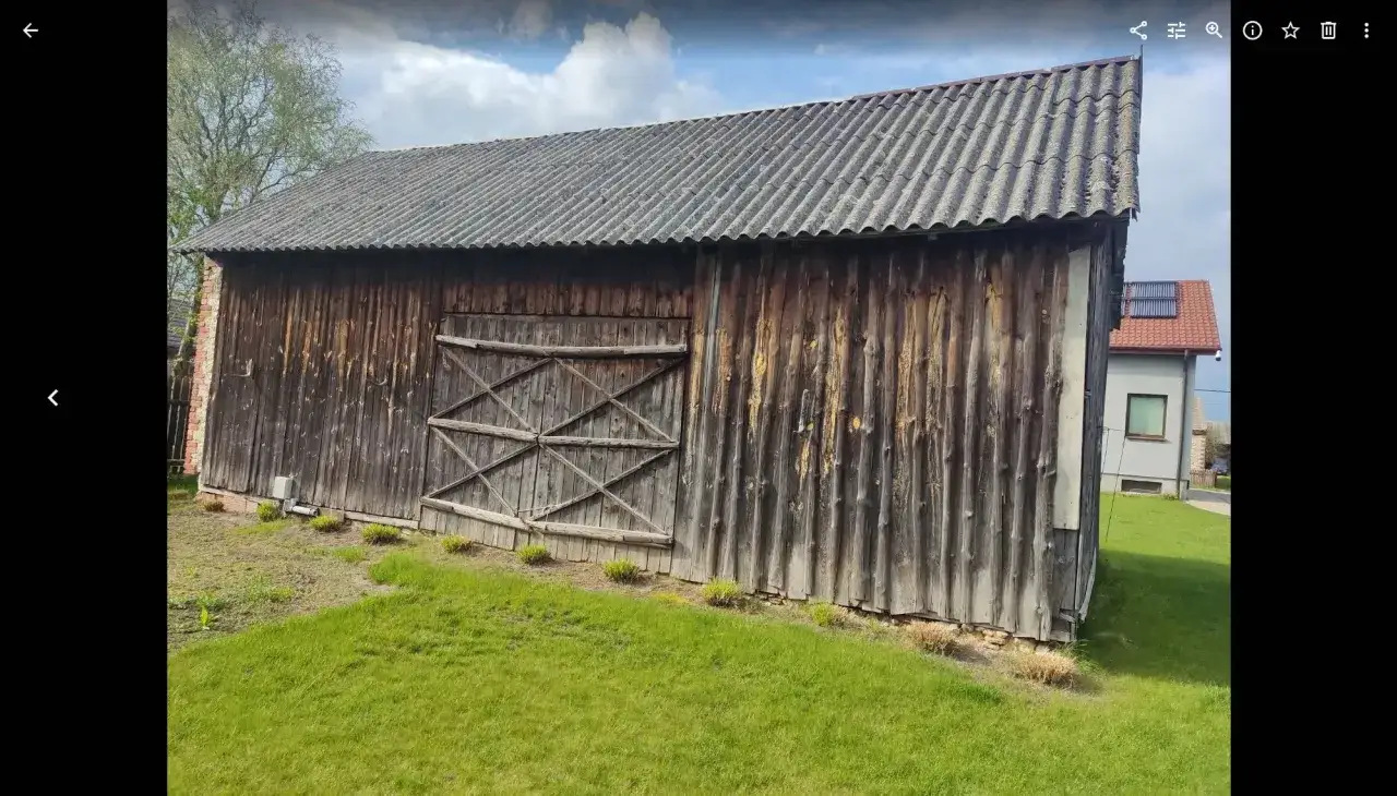 Stara drewniana stodoła z falistym dachem, obok dom. Zastanawiasz się, ile kosztuje wyburzenie stodoły?