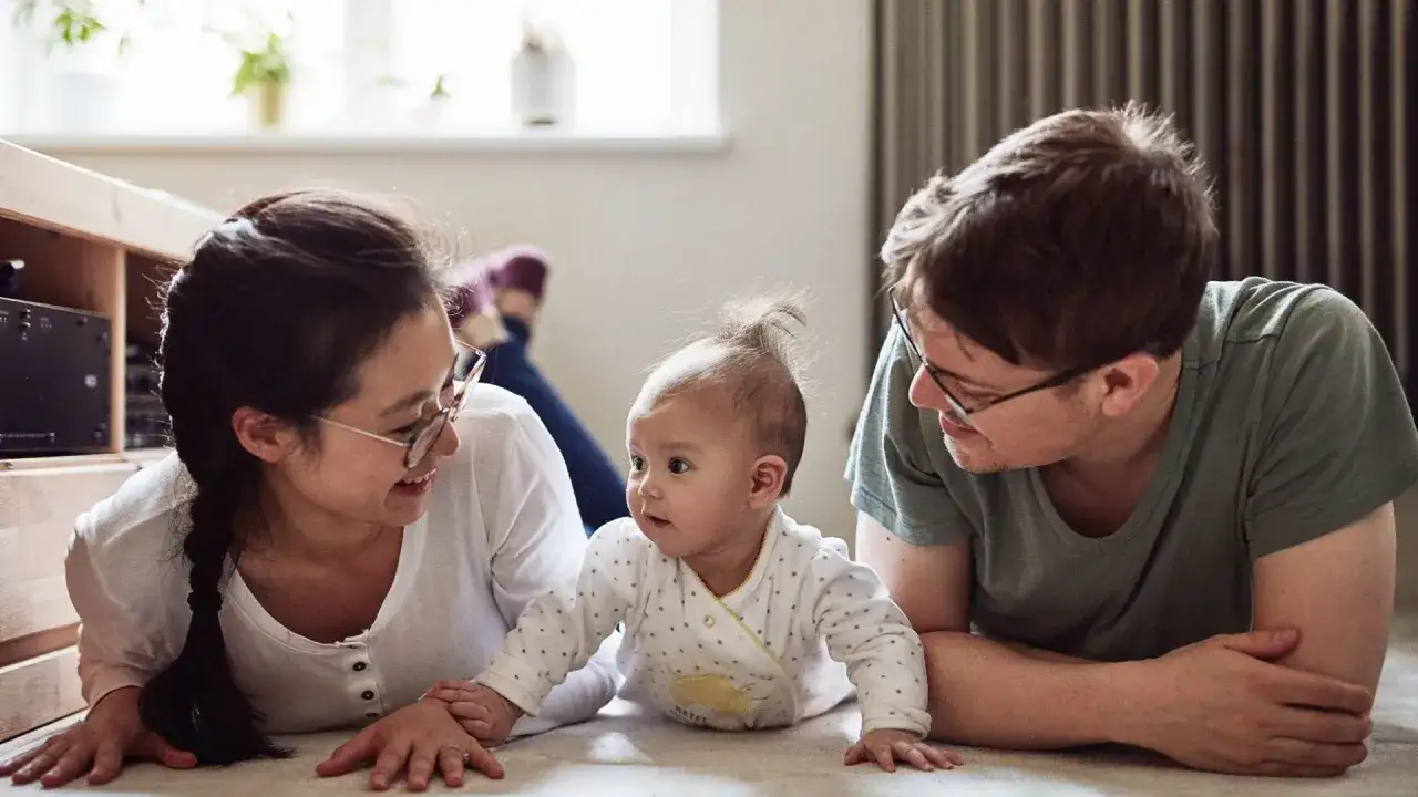 Gl&uuml;ckliche Familie mit einem **baby 3 monate** alt, das auf dem Boden krabbelt. Die Eltern schauen liebevoll auf ihr Kind.