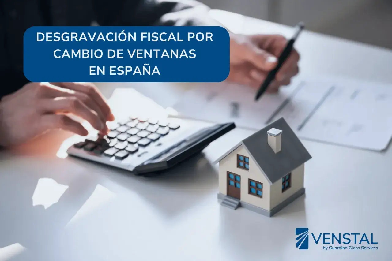 Manos calculando y escribiendo sobre cómo se puede desgravar el cambio de ventanas en España. Casa en miniatura y calculadora.