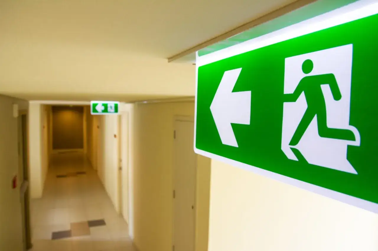 Gr&ouml;n n&ouml;dutg&aring;ngsskylt med pil &aring;t v&auml;nster. Viktigt f&ouml;r brandrutiner p&aring; arbetsplatsen.
