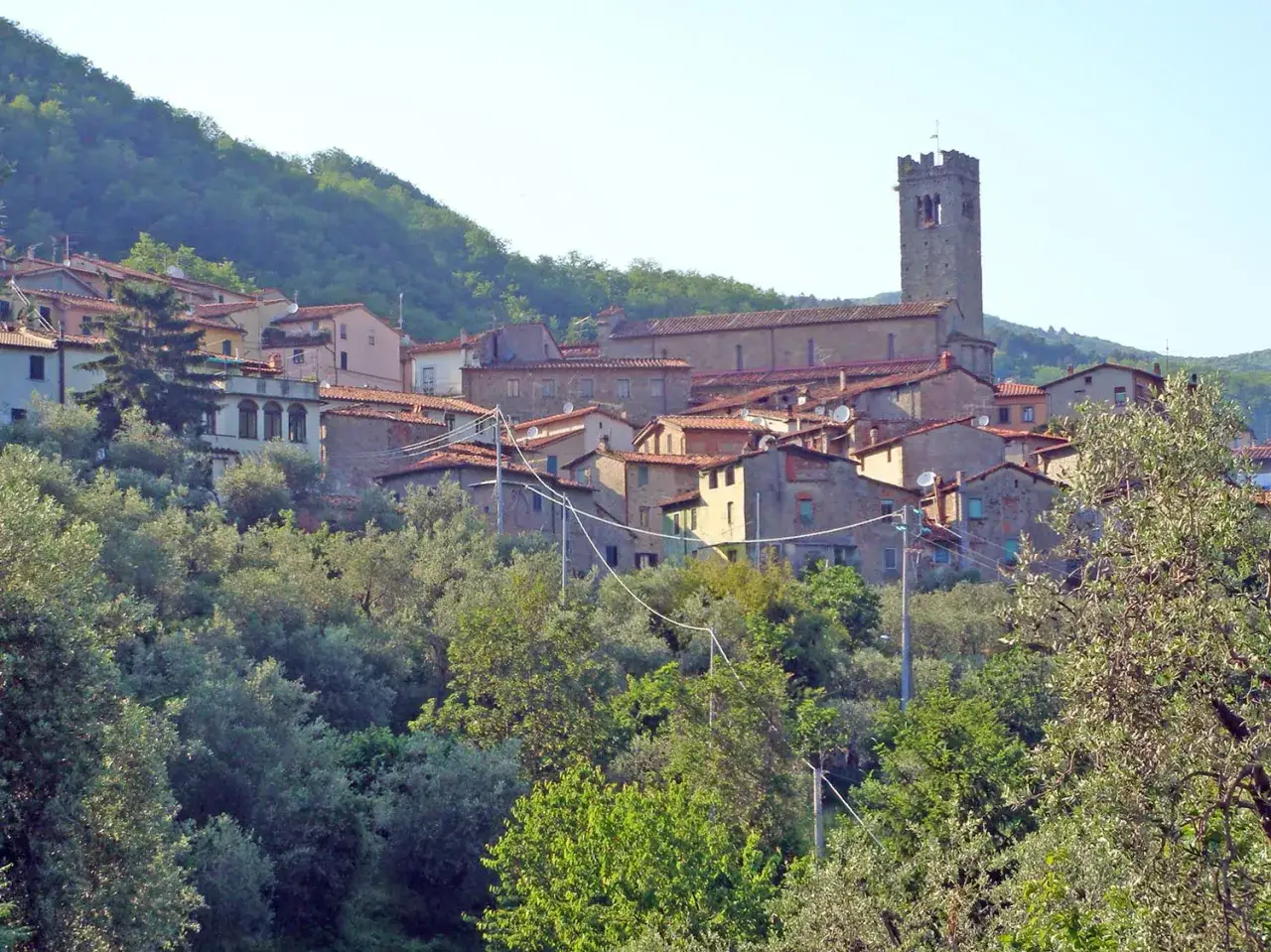 Un borgo collinare con case dai tetti rossi e una torre campanaria svetta, ricordando una antica villa basilica.