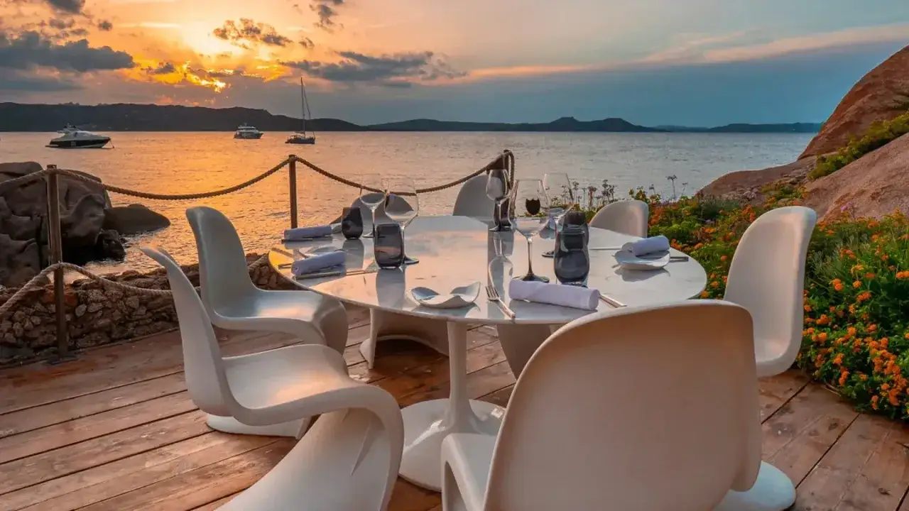 Tavola apparecchiata con vista sul mare al tramonto, un'esperienza indimenticabile all'Hotel Cala di Volpe.