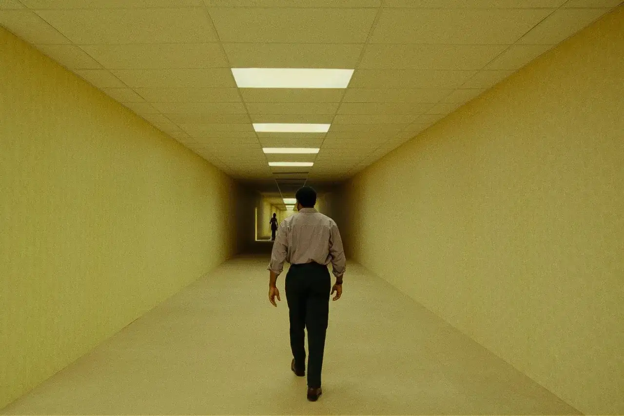 Un uomo cammina in un corridoio giallo infinito, un'immagine che evoca una scissione recensione. In lontananza, un'altra figura solitaria.