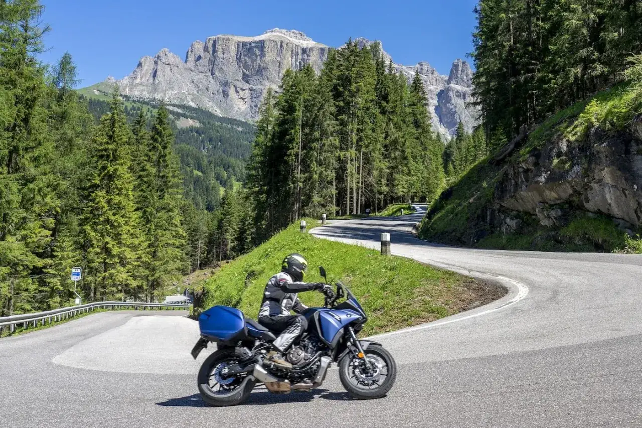 Motociclista affronta una curva su una strada panoramica tra i boschi del Veneto, con le maestose Dolomiti sullo sfondo. Un'avventura tra laghi e montagne in moto.