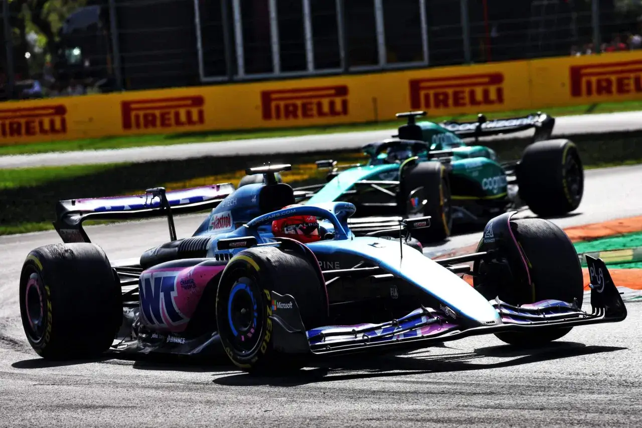 Zwei Formel 1-Autos rasen auf der Strecke, ein blau-pinkes Alpine und ein grünes Aston Martin. Die g-Kraft ist spürbar.