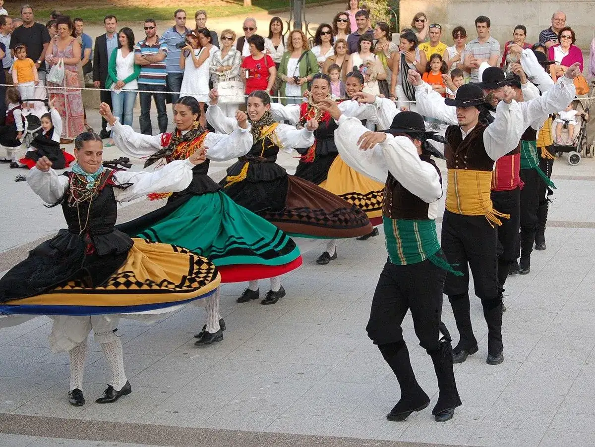 Un grupo de bailarines con trajes tradicionales españoles muestra que es la danza, con faldas amplias y chalecos coloridos.
