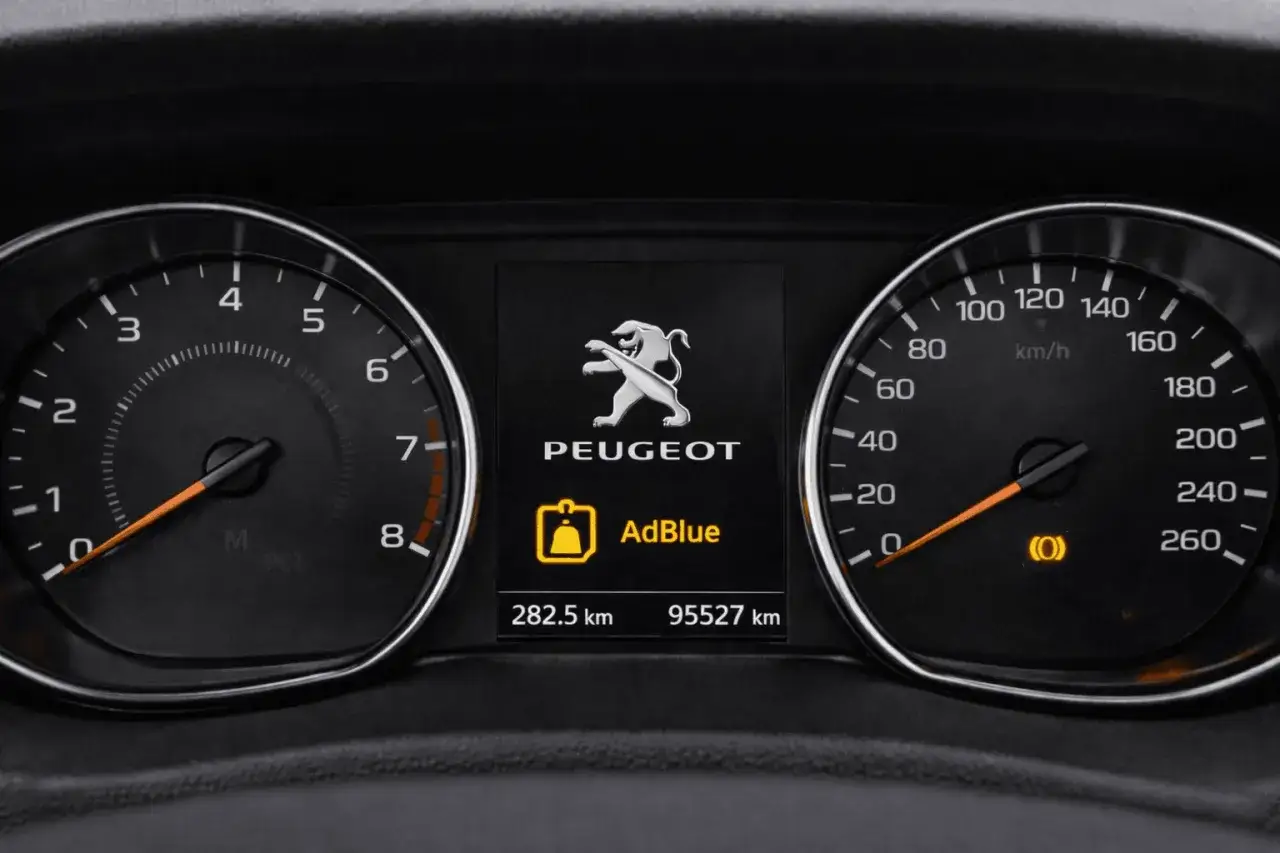Tableau de bord Peugeot avec le logo et un voyant AdBlue allumé. Le compteur indique 95 527 km.