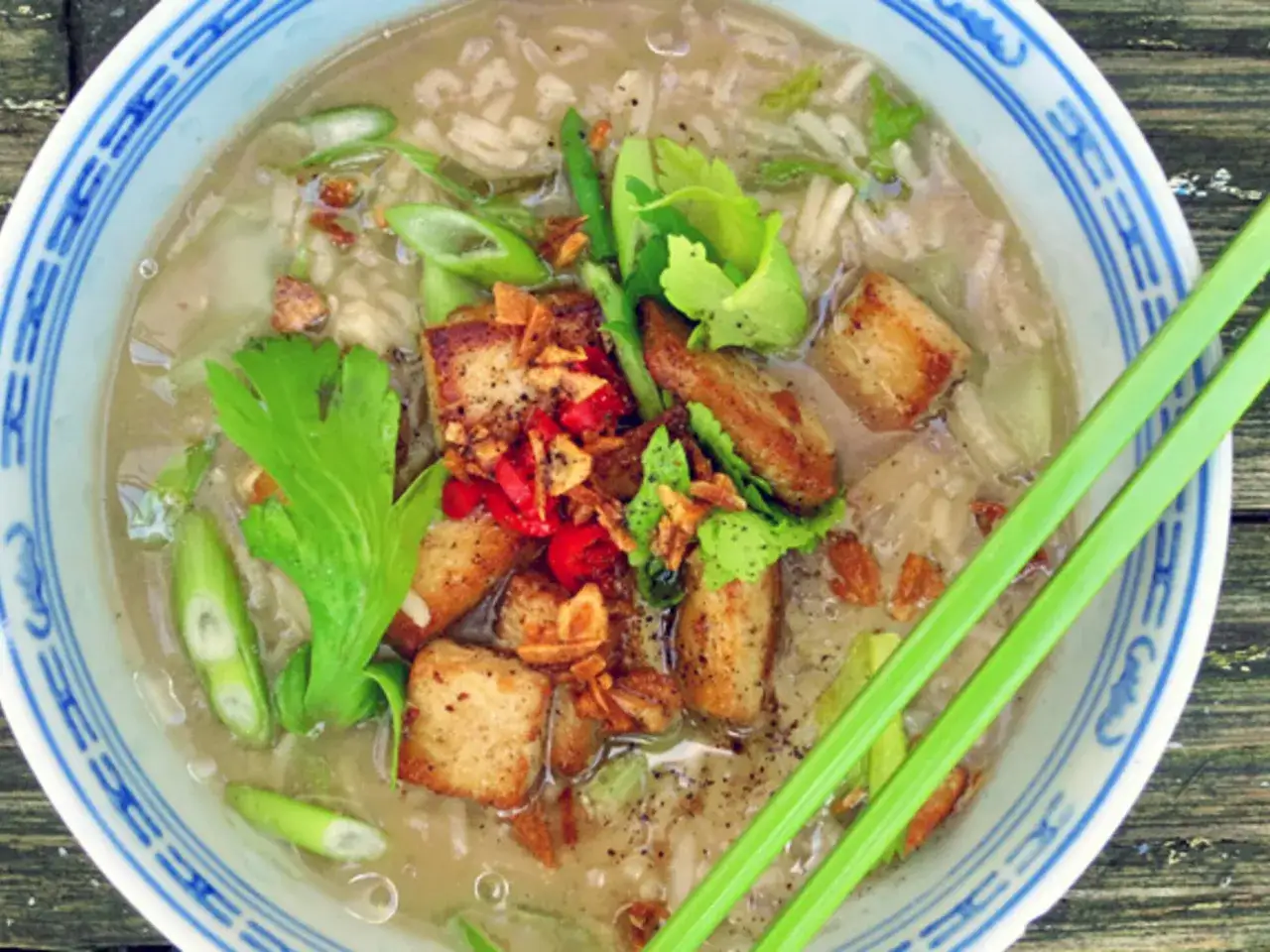 Khao tom: Eine Sch&uuml;ssel mit Reisbrei, garniert mit gebratenem Tofu, Fr&uuml;hlingszwiebeln und Kr&auml;utern.
