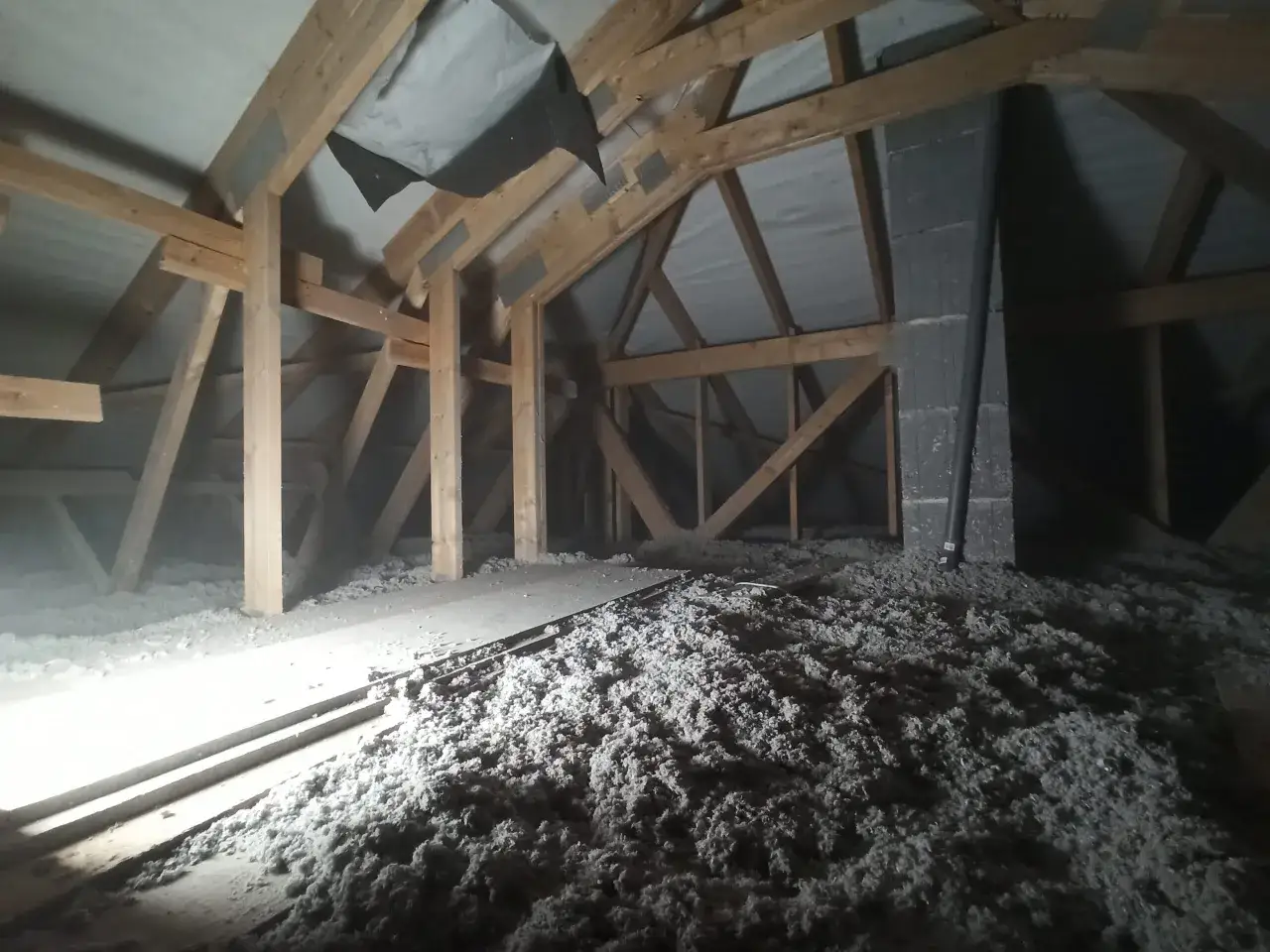 Strych z drewnianą konstrukcją i luźną izolacją, która może być celulozą. To materiał izolacyjny, który pomaga utrzymać ciepło.