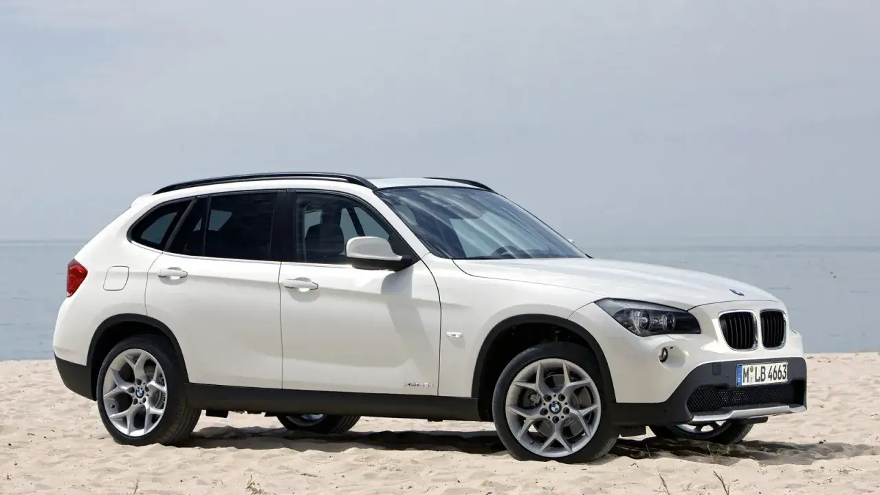 Białe BMW X1 na plaży, idealne na wakacyjne wypady. Zastanawiasz się, ile kosztuje BMW X1?