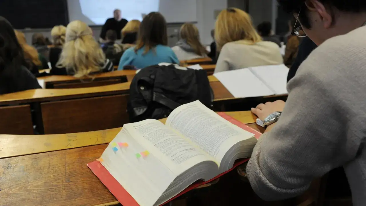 Ein Student im **Studium Jura** lernt in einer Vorlesung aus einem dicken Gesetzbuch.