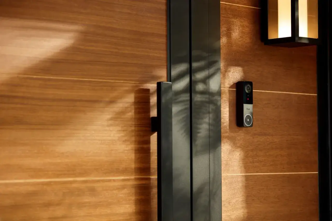Sonnette Philips WelcomeEye Connect 3 sur une porte en bois. Ombre de feuilles sur la porte.