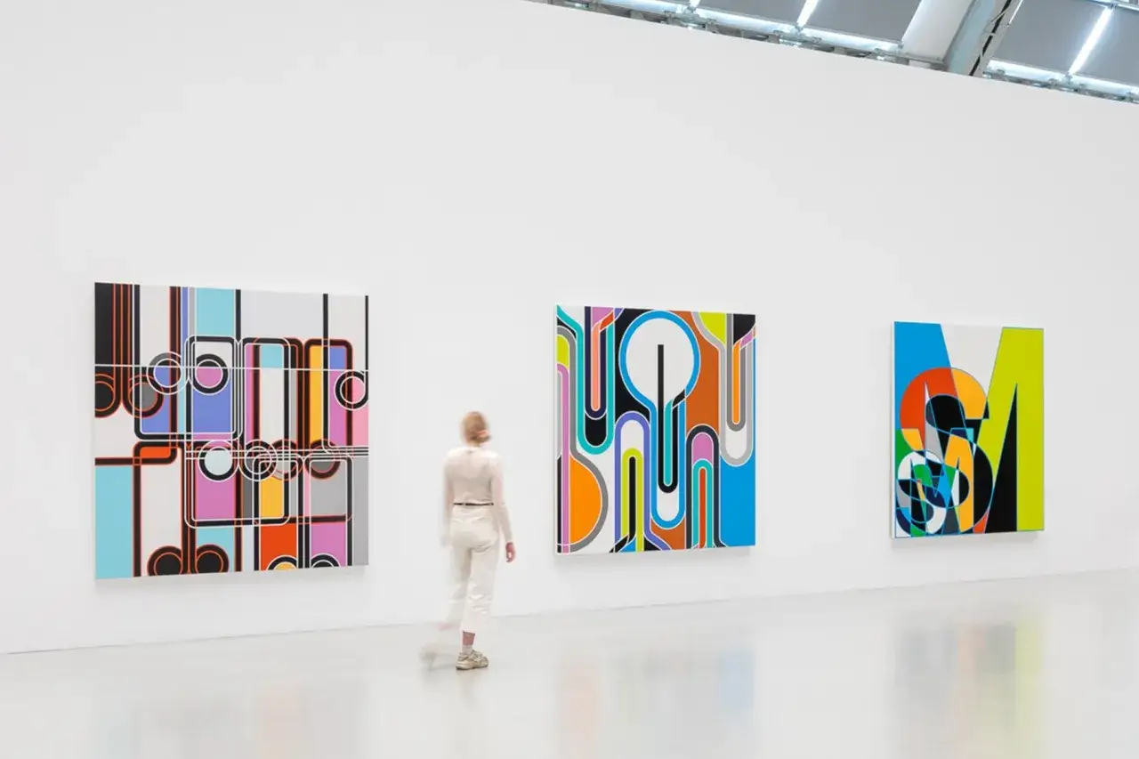 A person views colorful, geometric art pieces in a gallery, a testament to the evolving landscape of art finance.