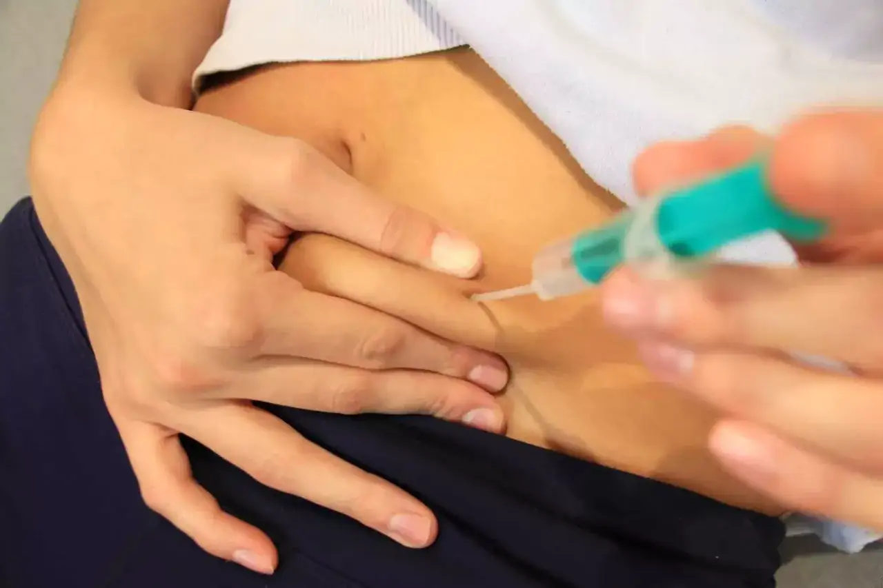 Eine Person führt sich selbst eine Spritze in den Bauch. Dies ist eine wichtige Maßnahme, um eine Thrombose nach einer Operation zu verhindern.