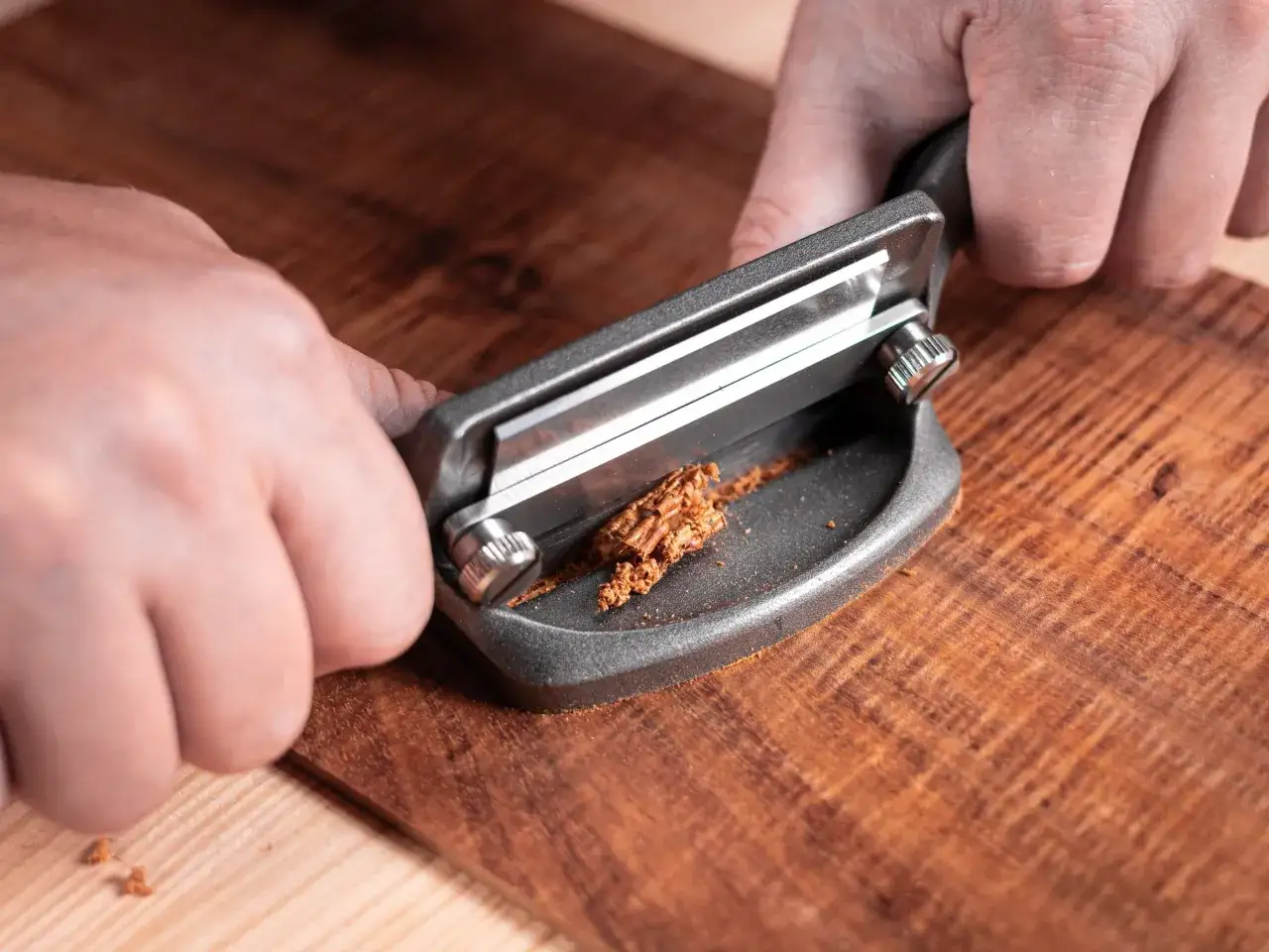 Mani che usano una pialla per rimuovere trucioli di legno, mostrando come sverniciare il legno per un restauro perfetto.