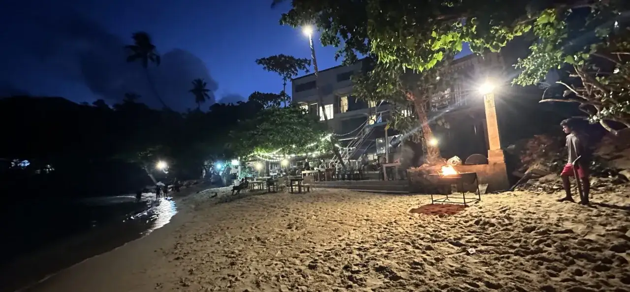 Wieczór na plaży w Mirissa Sri Lanka. Ognisko, palmy i restauracja oświetlona girlandami.