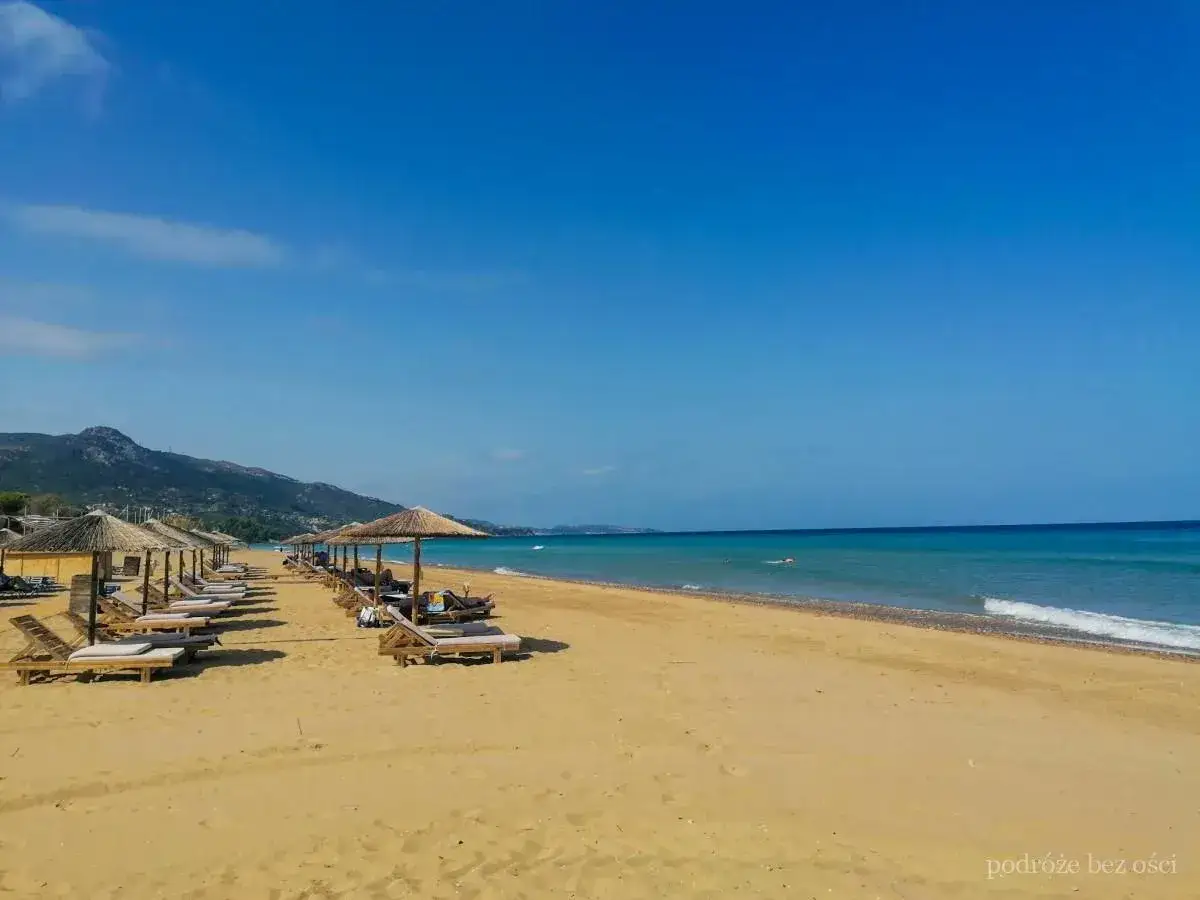 Piękne zakynthos plaże z rzędami leżak&oacute;w i parasoli. Czysta, błękitna woda i g&oacute;ry w tle tworzą idealny krajobraz.