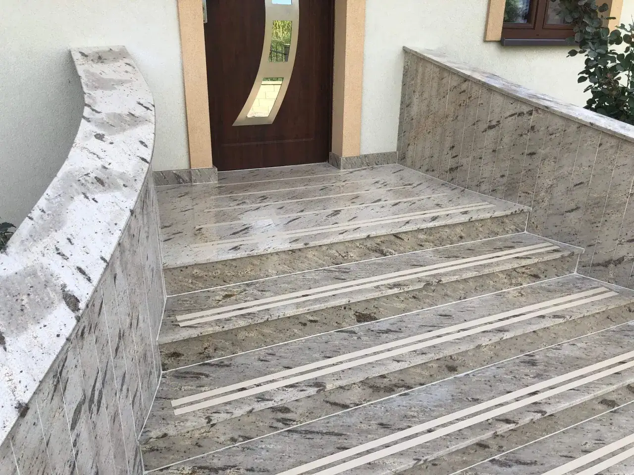 Eleganckie schody z kamienia naturalnego, z antypoślizgowymi paskami, prowadzą do drzwi wejściowych.