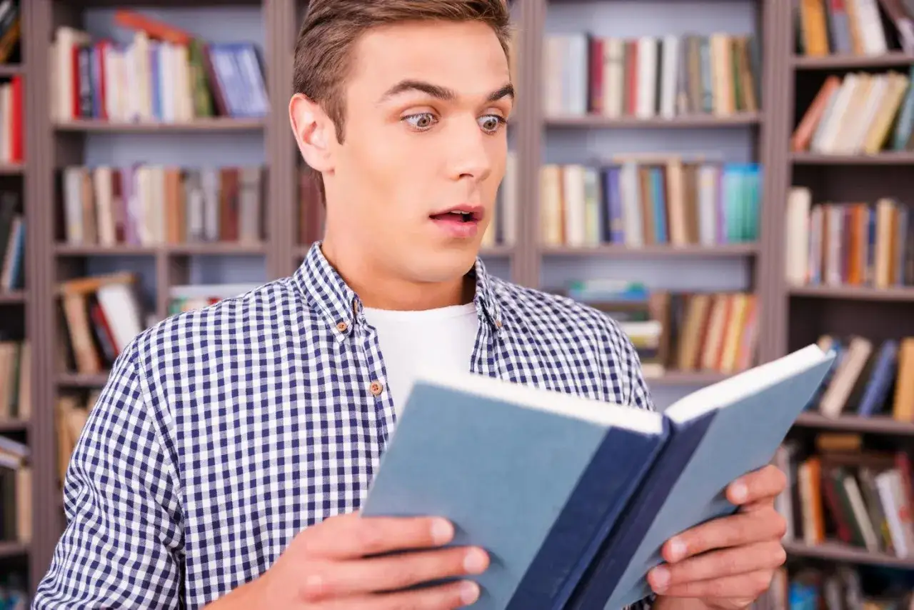 Joven sorprendido leyendo libros para 13 a&ntilde;os en una biblioteca.