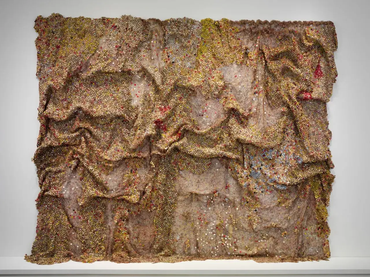&OElig;uvre d'El Anatsui, une tapisserie textur&eacute;e de bouchons de bouteilles en aluminium, aux reflets dor&eacute;s et cuivr&eacute;s, &eacute;voquant des vagues ou des plis de tissu.