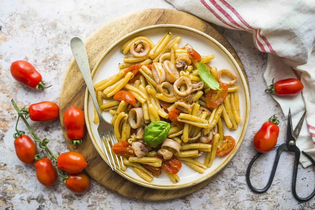 Piatto di pasta con calamari, pomodorini e basilico, pronto per essere gustato.