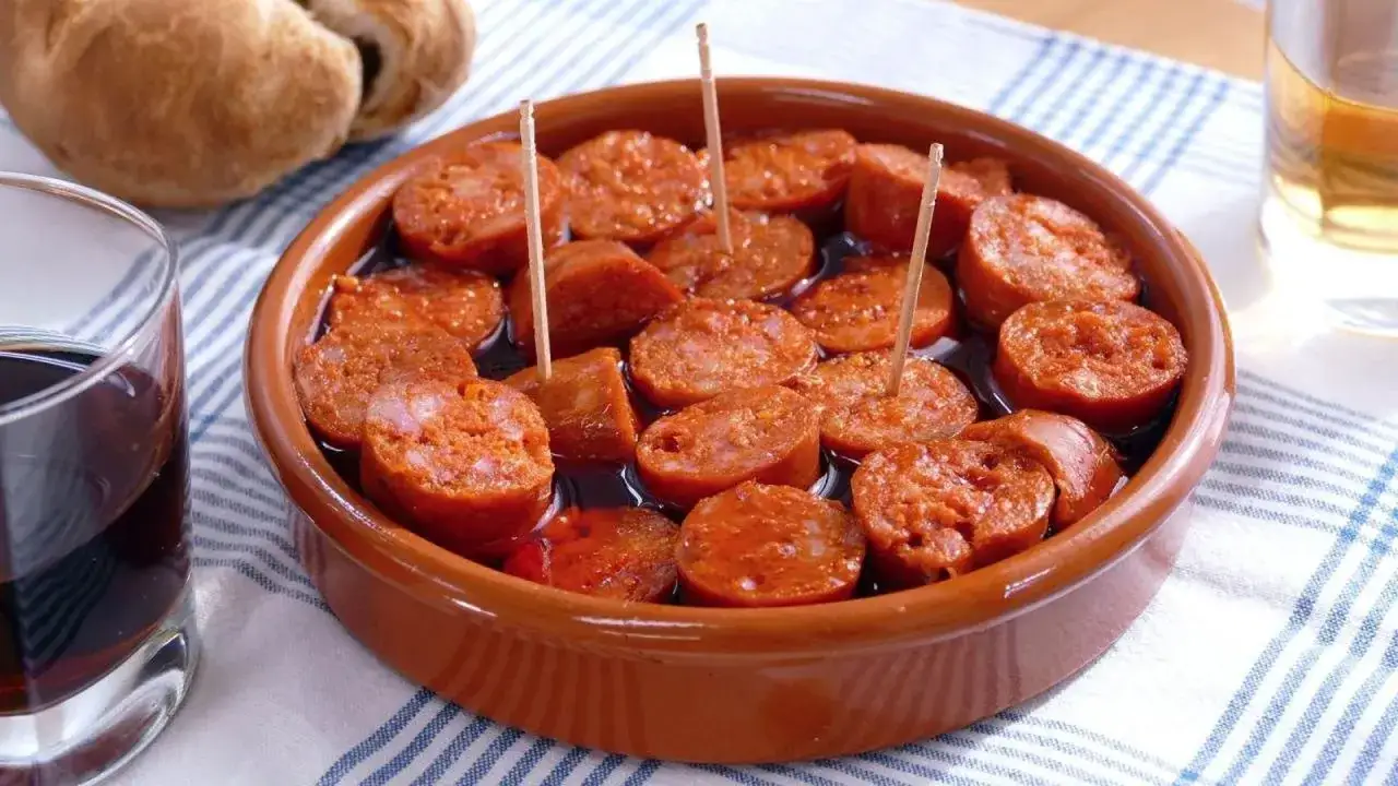 Tapa de chorizo a la sidra, servido en cazuela de barro con palillos. Acompañado de pan y copas de vino.