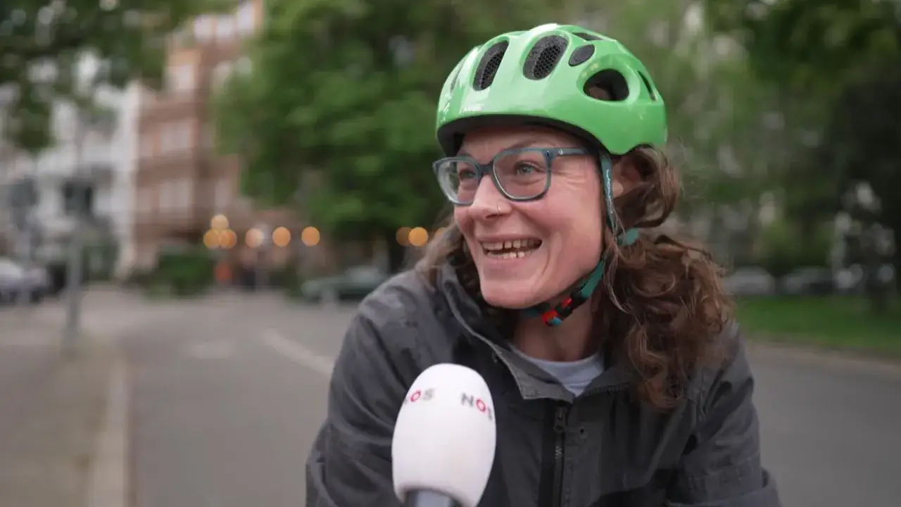 Vrolijke vrouw met groene fietshelm en bril, vertelt over de fietshelm verplicht in Duitsland.