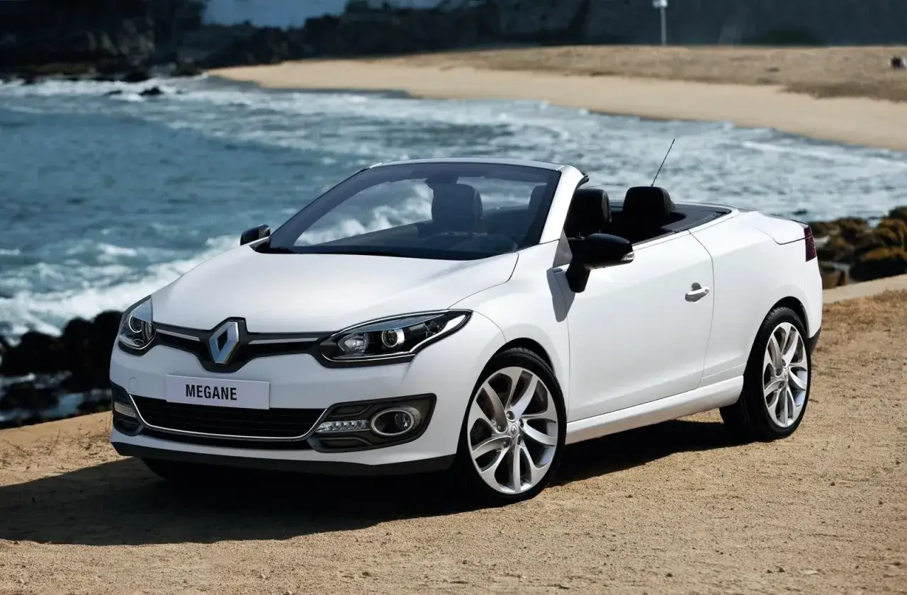 Biały Renault Megane cabrio na plaży, z morzem i piaskiem w tle. Idealny na letnie przejażdżki.
