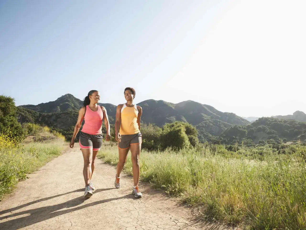 Due donne camminano su un sentiero in collina, il loro passo leggero riflette il significato di un'andatura sana e felice.