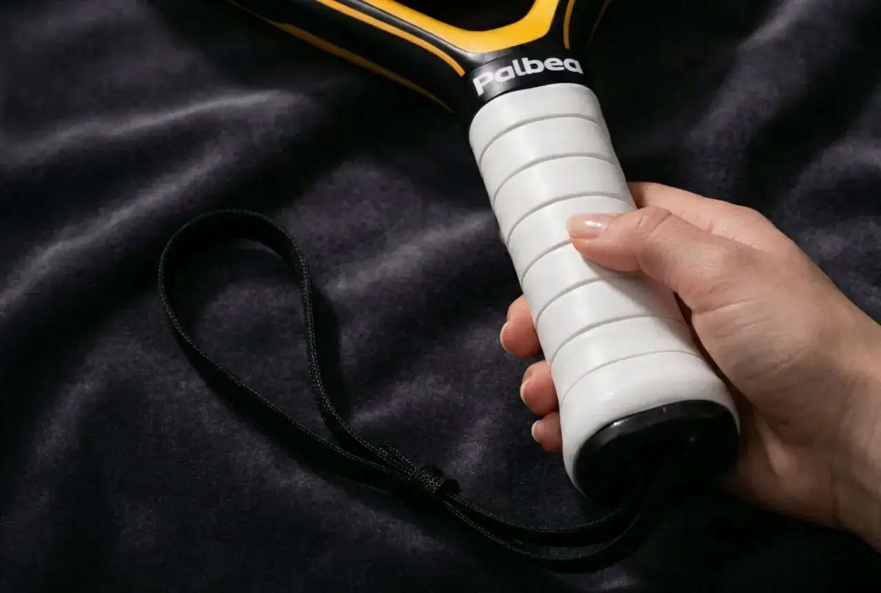Mano che impugna la racchetta Palbea, mostrando il grip bianco e il laccetto. La differenza tra grip e overgrip &egrave; fondamentale per una presa salda.