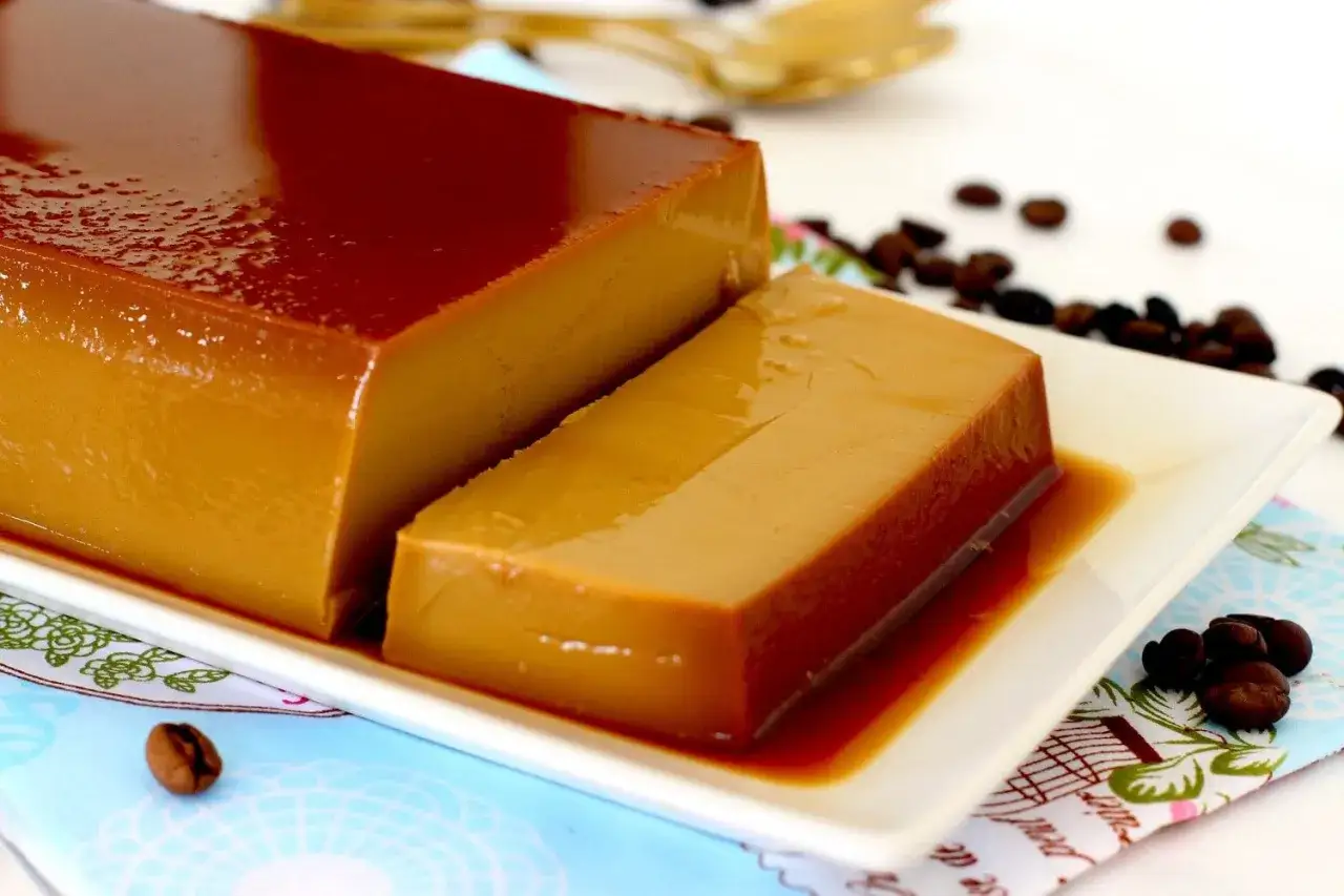 Un delicioso flan de café, con su caramelo brillante, servido en una bandeja blanca, rodeado de granos de café tostado.