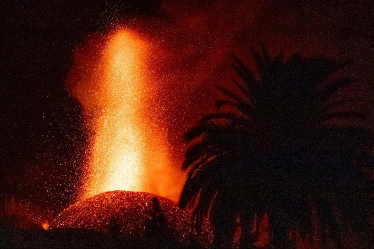 Erupcja wulkanu na La Palmie, z fontanną lawy i popiołu, w cieniu palmy. Obraz budzi grozę, jakby zapowiadał tsunami.