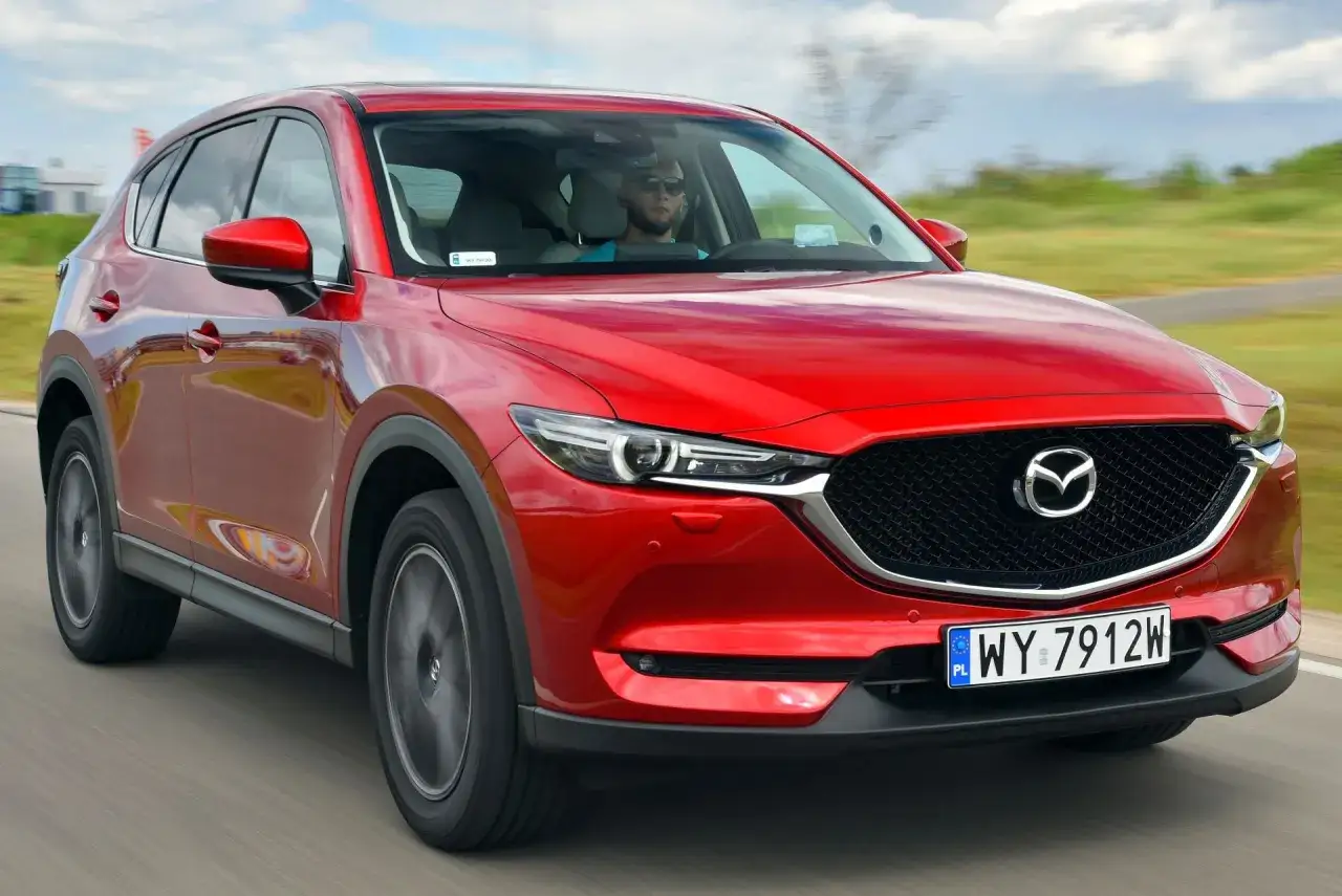 Czerwona Mazda CX-5 w ruchu. Kierowca w okularach przeciwsłonecznych. Czy negatywne opinie o tym modelu są uzasadnione?